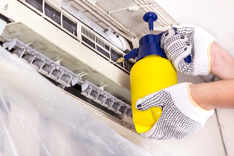 Technician spraying chemical water onto air conditioner grid to clean