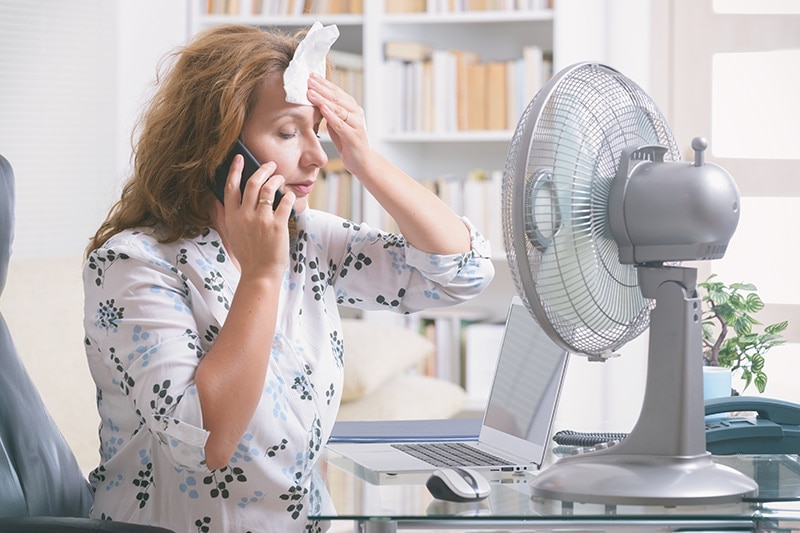 When Do I Replace My Air Conditioner? Woman cooling off in front of a fan.