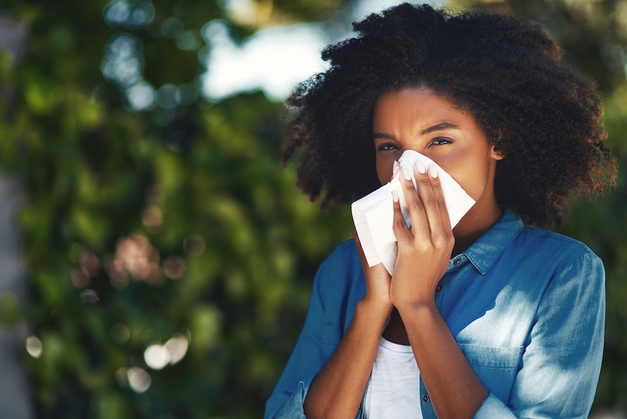 Portrait of a young woman blowing her nose with a tissue outside.